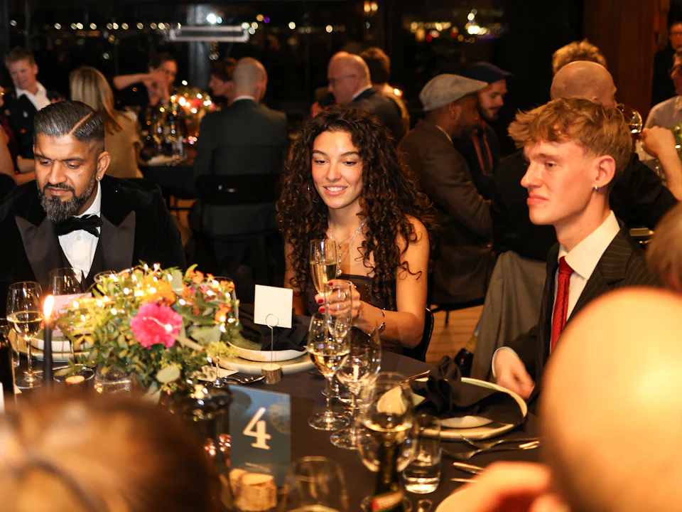 Guests in black tie at a round table with candles, flowers and table number four at a formal dinner